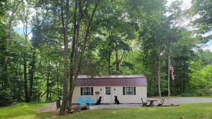 A cabin with a metal roof, surrounded by trees, and two blue chairs in front. - Glamping Clear Spring Maryland 
3-Cabin Campground (Clear Spring)