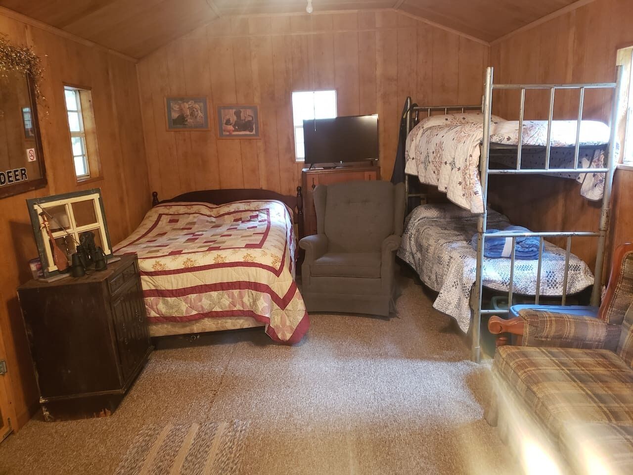 A cozy room with a wooden interior, a bed with a quilt, a chair, a bunk bed, and a television.