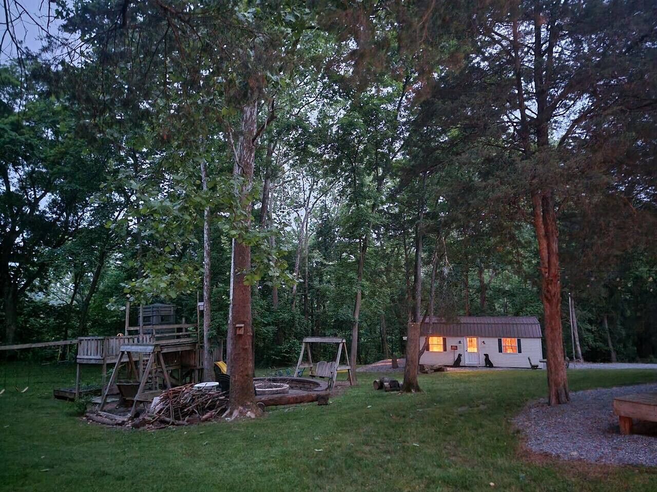 A rustic cabin surrounded by dense trees, with a swing set and a wooden deck.