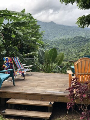 Eine Holzterrasse mit Liegestühlen und einem Picknicktisch, mit Blick auf ein üppiges, grünes Tal und Berge.