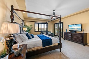 Una cama con dosel, un televisor y un aparador en una habitación luminosa con ventanas amplias.