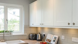 A modern kitchen with white cabinets, a stainless steel sink, a toaster, a kettle, and a cookbook on the counter.