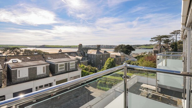 A residential area with a view of the sea, a clear sky, and a modern building with a glass balcony.