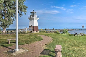 Ein Leuchtturm mit einem Ziegelweg, Bänken und Picknicktischen am Wasser.