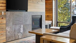Een moderne woonkamer met een open haard, houten lambrisering, een bank en een eettafel.