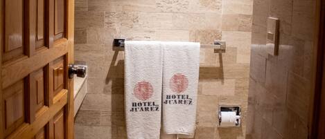 Un baño de hotel con pared de piedra, dos toallas colgadas en un perchero y una puerta de madera.