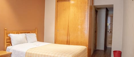 Une chambre à coucher avec un lit en bois, une armoire et un seau rouge.