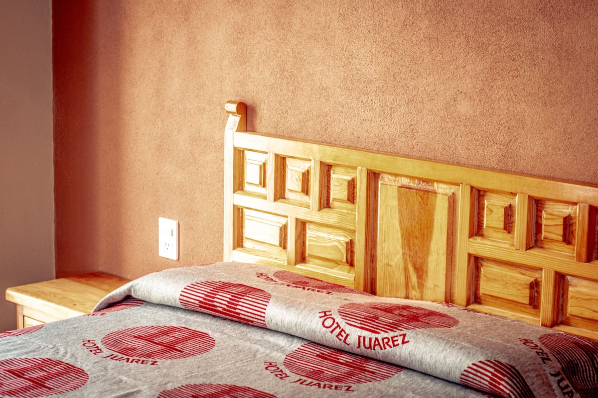 A bed with a wooden headboard and a pillow with 'HOTEL JUAREZ' printed on it.
