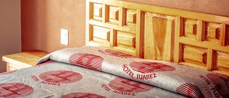 A bed with a wooden headboard and a pillow with 'HOTEL JUAREZ' printed on it.