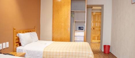 A hotel room with two beds, a wooden headboard, a wardrobe, a small desk, and a red trash bin.