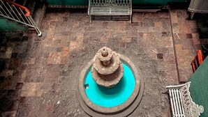 A courtyard with a fountain at the center, surrounded by stone tiles and a green wall. - Hotel Juarez (Mexico City)