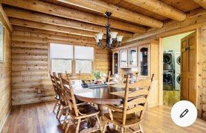 A wooden log cabin interior with a dining table and chairs, a chandelier, and a view of a washing machine. - Angela Custom Log House<br>on 7 acres. <br>Pets Not Allowed. <br>No Smoking. (Robertsville)