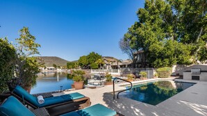 A poolside area with lounge chairs, a pool, and a view of a hill and trees.