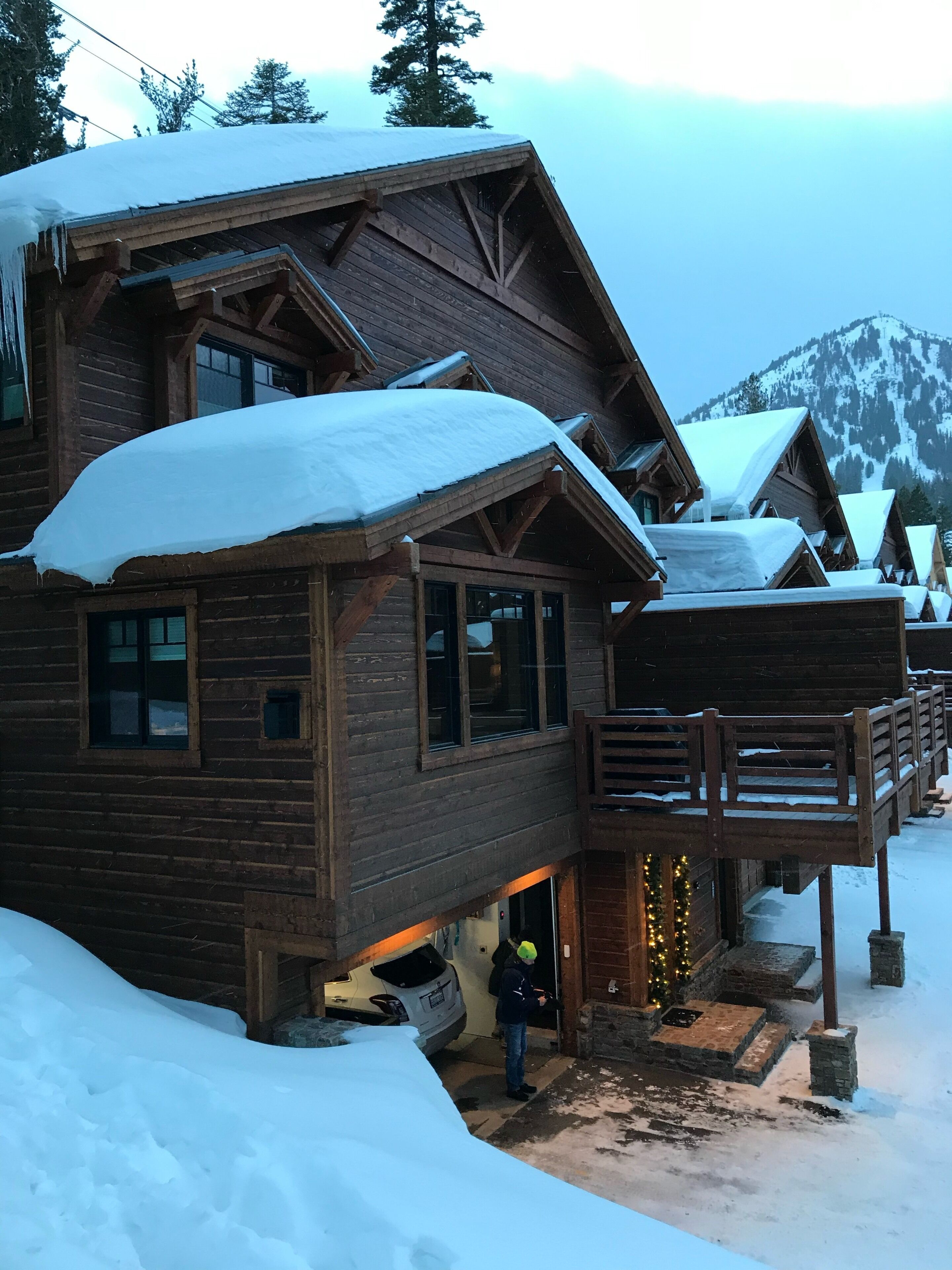 Un chalet en bois, dont le toit est recouvert de neige, et qui possède un balcon illuminé.