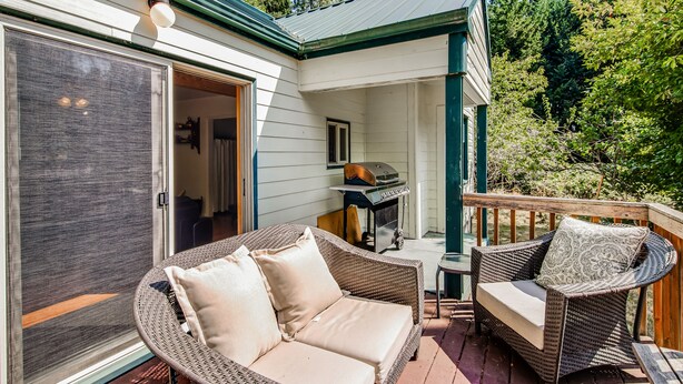 Une terrasse couverte, meublée avec des meubles en osier, dotée d’un barbecue et d’une porte-fenêtre coulissante.