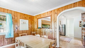Une pièce aux murs lambrissés, comprenant une table et des chaises, un coin cuisine avec un réfrigérateur, et un mur en briques.