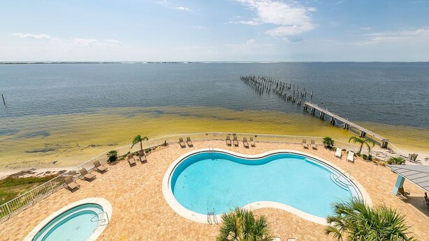 A swimming pool with a view of the ocean and a pier extending into the water. - Amazing Views from this waterfront condo. (Pensacola)