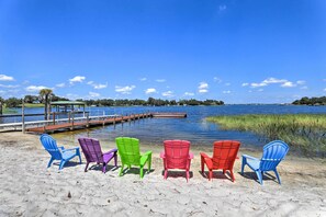 A beach with colorful Adirondack chairs facing a calm lake, a dock extending into the water, and a clear blue sky. - Lakefront Babson Park Escape: Pet Friendly! (Babson Park)