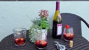 Een rieten tafeltje met twee glazen rode wijn, een fles wijn, een kleine potplant en een kurkentrekker.