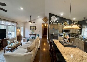 A spacious living room with a large sofa, a coffee table, and a television. The kitchen features a granite countertop, stainless steel appliances, and pendant lighting. - Three Kings (Oriskany Falls)