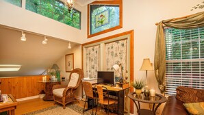 Una sala de estar acogedora con piso de madera, un comedor con sillas de mimbre, un escritorio con computadora y un sofá confortable.