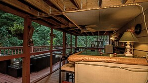 Una terraza de madera con un jacuzzi, asientos acolchados y un ventilador de techo.