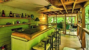 Una zona rústica con barra de madera, un ventilador de techo, una barra y taburetes.