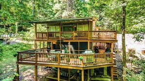 Una cabaña de madera de dos pisos con balcón, rodeada de un bosque denso.