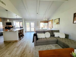 A spacious living area with a grey sectional sofa, a wooden coffee table, and a kitchen area with white cabinets and a flat-screen TV. - Clean and Neat. Full home. Pet friendly (Garland)