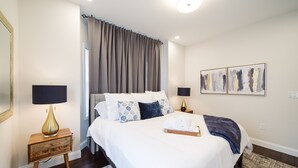 Une chambre à coucher avec un lit, deux tables de chevet, une lampe, un miroir et des œuvres d’art accrochées au mur.