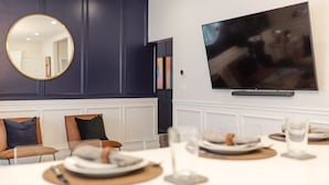 Un coin repas avec une table dressée pour quatre personnes, un miroir rond, des panneaux muraux bleu foncé et un téléviseur à écran plat fixé au mur.