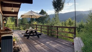 A wooden deck with a picnic table and umbrella, surrounded by a wooden railing and overlooking a forested mountain area. - Escape To The Hacienda (Ben Lomond)