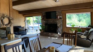 A cozy living room with a fireplace, wooden ceiling, and large windows. - Escape To The Hacienda (Ben Lomond)