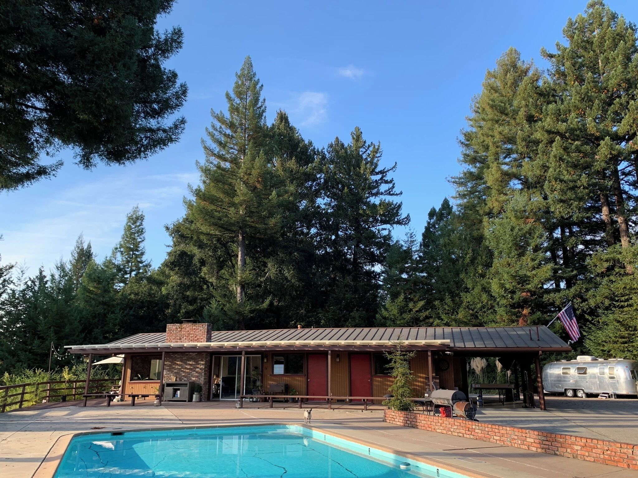 A pool area with a covered patio, a barbecue grill, and an American flag.