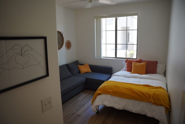 A bedroom with a bed, a sofa, a window, and a framed artwork on the wall.