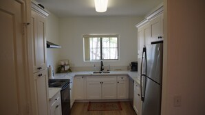 A kitchen with white cabinets, a stainless steel refrigerator, a stove, and a window above the sink.