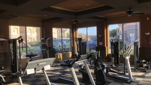 A gym with treadmills, ellipticals, and weight machines, large windows with a view of buildings and parked cars.