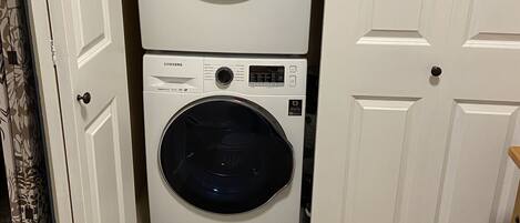 A laundry room with two stacked washers and dryers, a blue detergent bottle, and a door leading to another room.