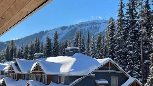 A row of cabins with snow-covered roofs and a clear blue sky. - Townhouse backing onto the skating loop (Apex Mountain, Penticton)