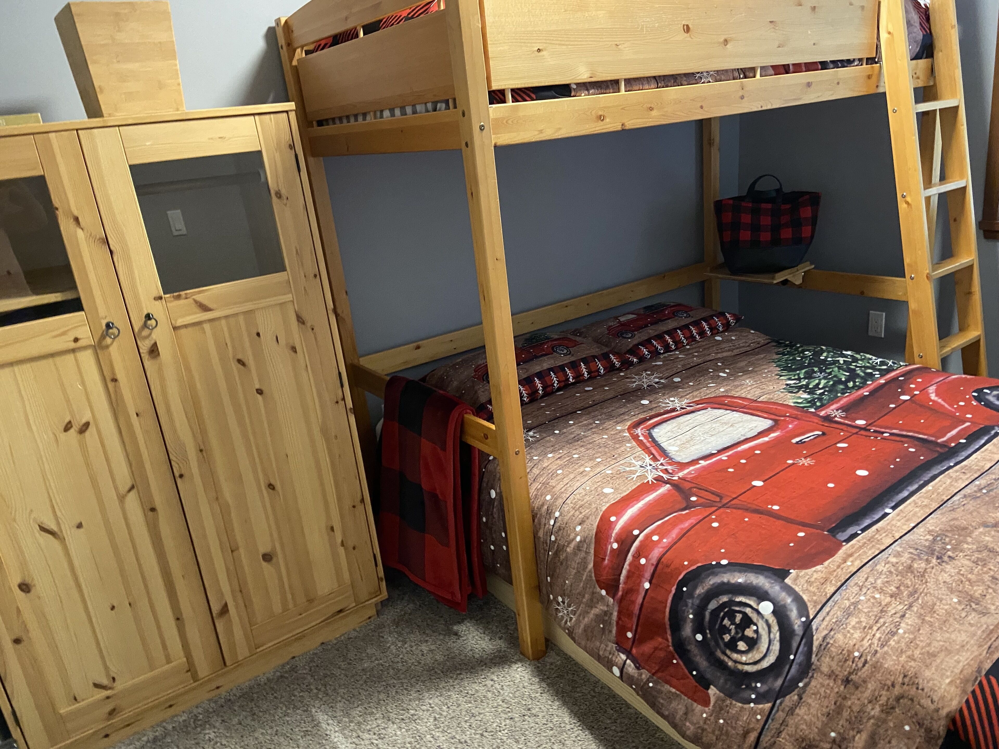 Una cama individual superpuesta con edredón de temática automovilística, un armario de madera y una escalera.