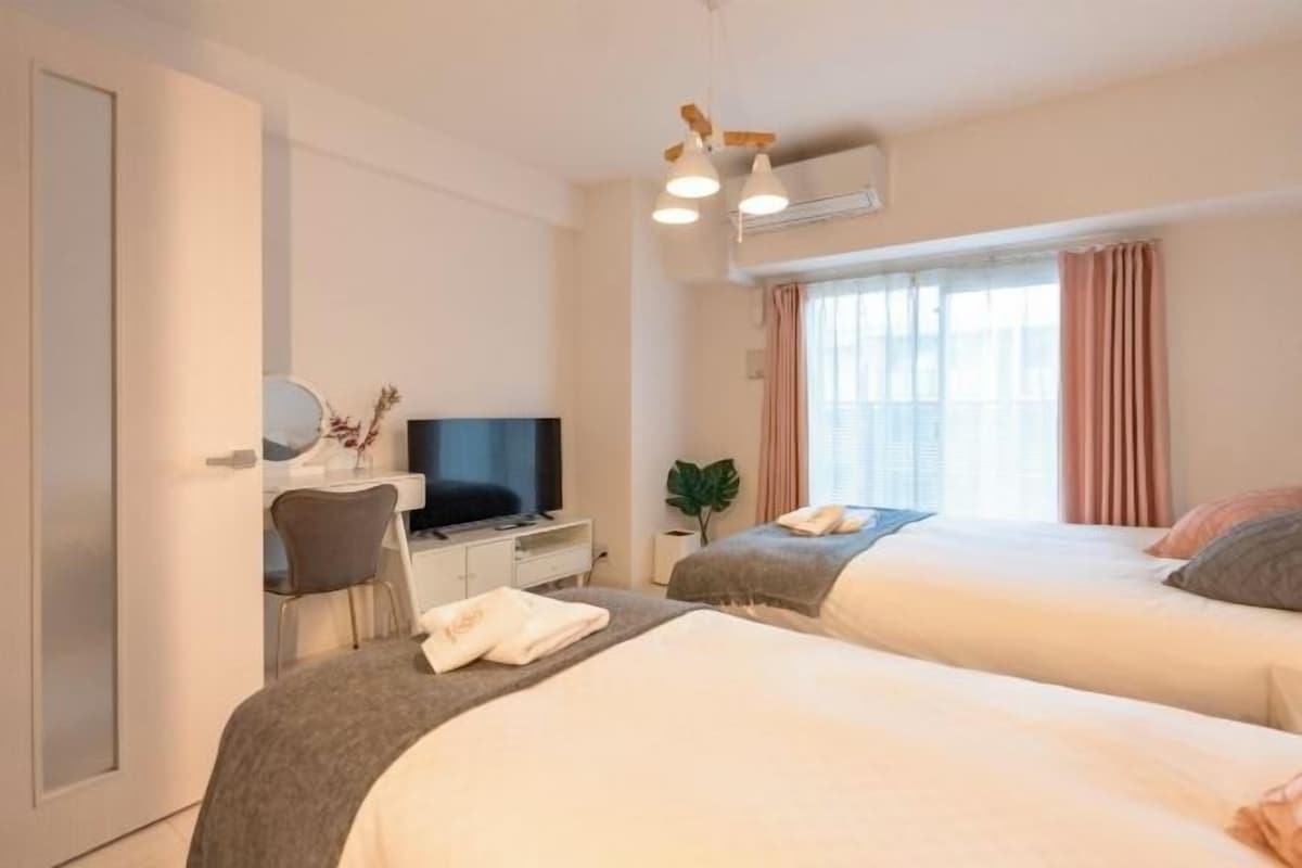 A hotel room with two beds, a desk with a TV, a chair, and a window with curtains.