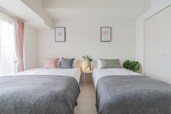 A bedroom with two beds, a small table with a vase, and a plant.