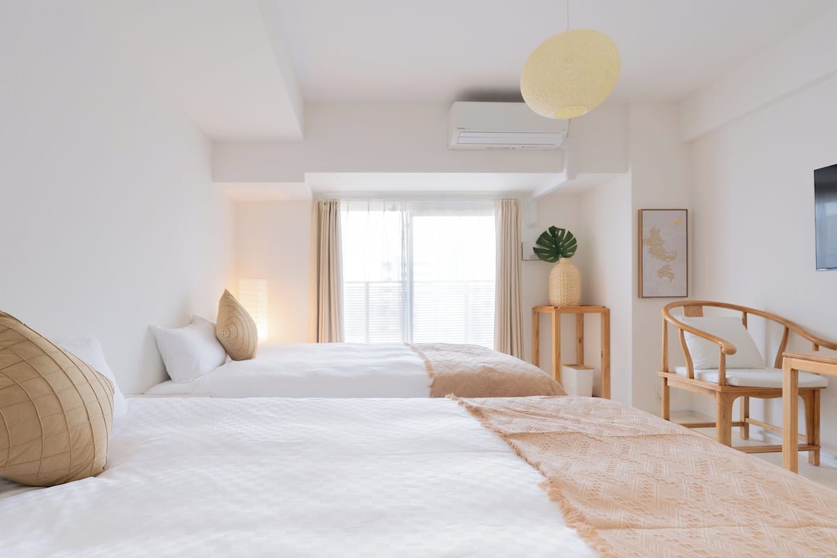 A modern hotel room with two beds, a large window, a ceiling fan, and a wooden chair.