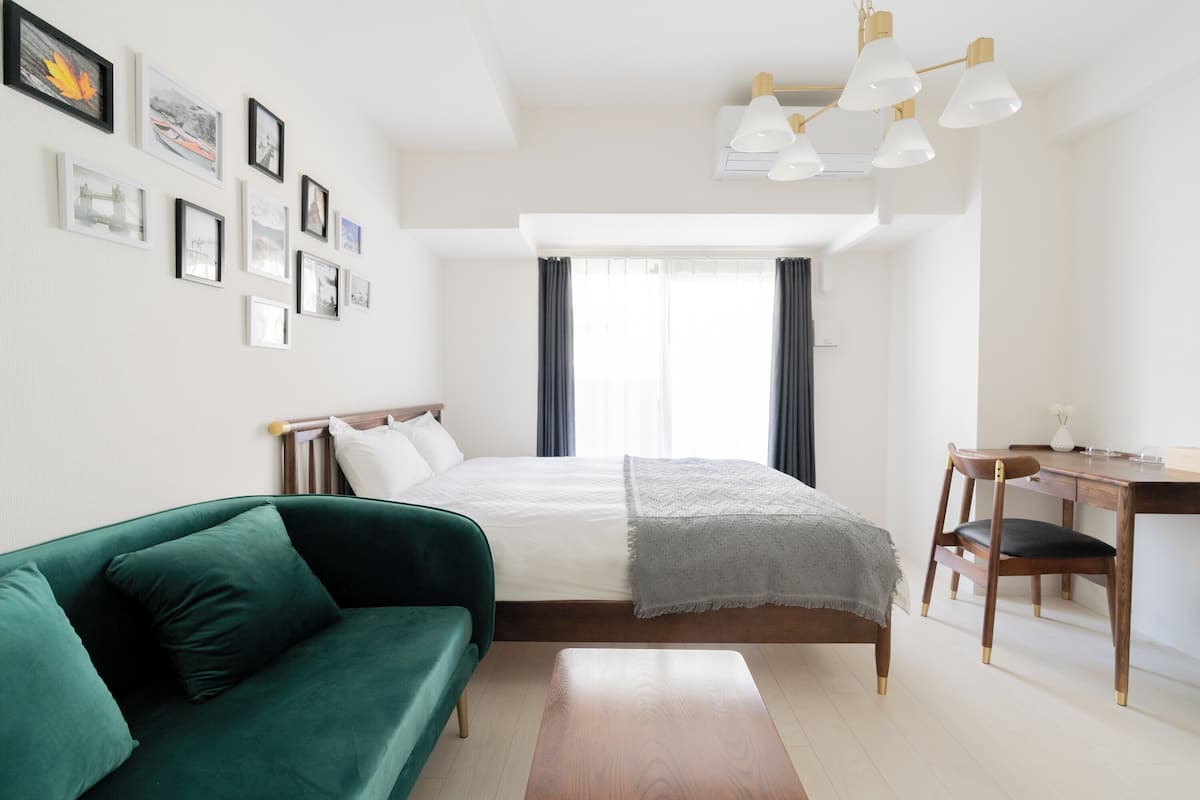 A modern bedroom with a bed, a green sofa, a wooden desk, and a wall with framed pictures.