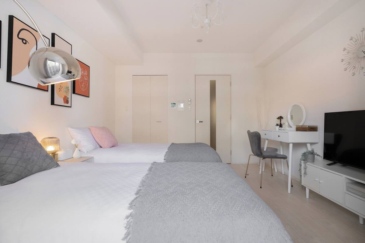 A modern bedroom with two beds, a desk, a TV, and artwork on the walls.