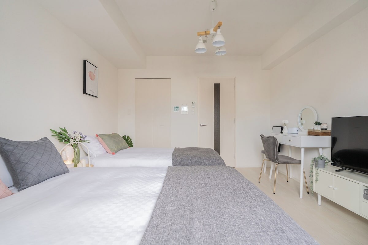 A modern hotel room with two beds, a desk, a TV, and a small plant.