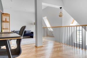 Relax in this spacious loft-style room with a high ceiling and sloped design, featuring a wooden floor and comfortable seating areas.