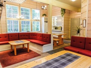 A cozy interior with a red sectional sofa, a wooden table, and a kitchen area visible through an open door. - Porukka 1 by Interhome (Kittilä)