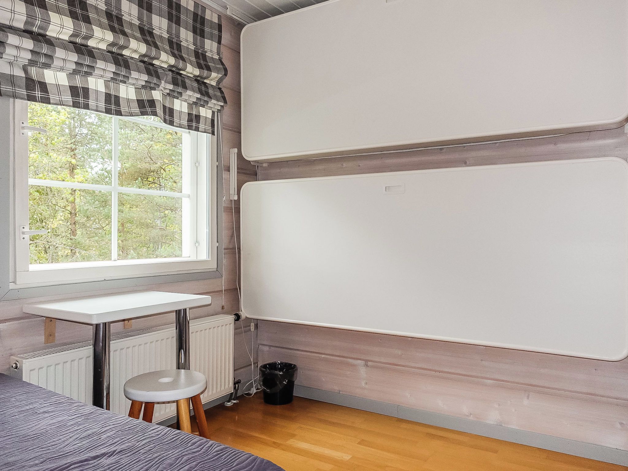 A room with a window, a radiator, a whiteboard, a small stool, and a radiator cover on the floor.
