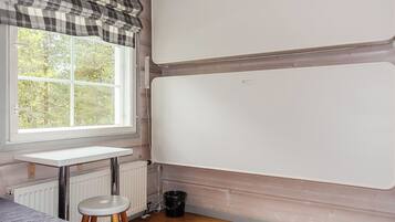 A room with a window, a radiator, a whiteboard, a small stool, and a radiator cover on the floor.
